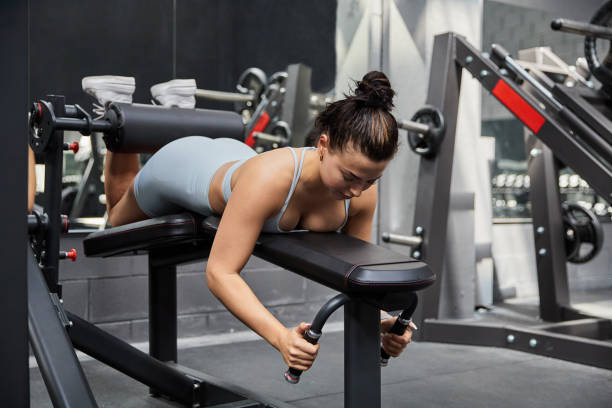 istock Strong ethnic sportswoman lying on chest and doing exercises on hamstring curl machine in gym 1694186336
