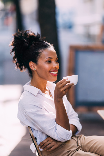 A side view of a smiling Latin female (looking away) holding a cup of coffee while relaxing outdoors.