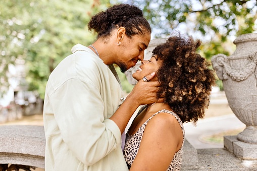 Multiracial man kissing his girlfriend in the park