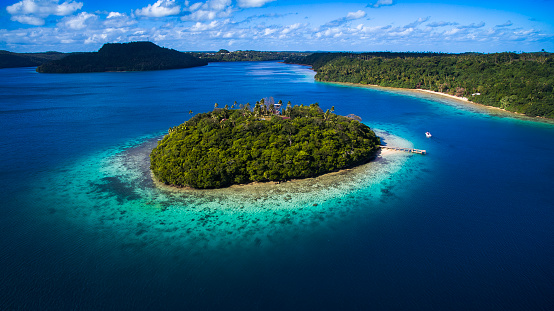 Aerial view of tropical island surrounded by pristine blue water and coral reef in Tonga