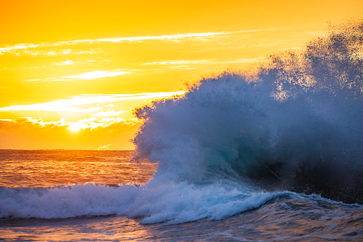Silhouetted ocean waves breaking with vivid golden sunrise. Photographed on the south east coast of Australia.