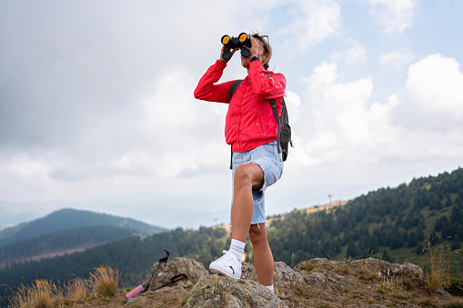 From the observation point on the mountain, a young Caucasian female hiker observing nature with binoculars