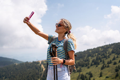 Active young Caucasian woman taking selfie with mobile phone, during her hike on the mountain