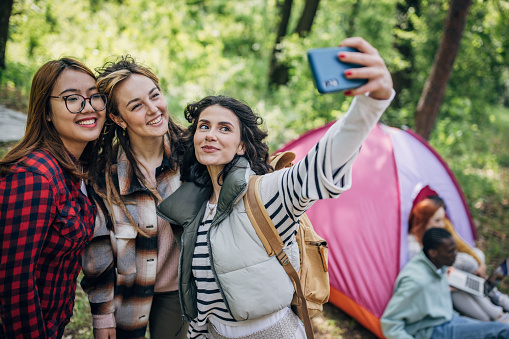 Multi-racial group of friends, female hikers using smart phone for selfie together in nature.