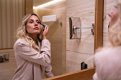 Caucasian woman applying mascara, while observing herself in the bathroom mirror
