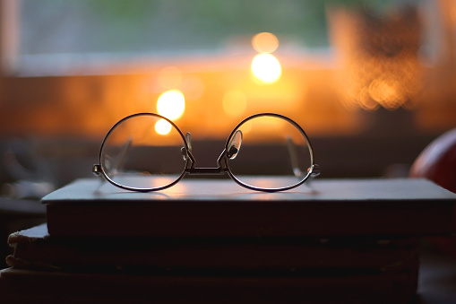 Vintage books, reading glasses, cup of tea or coffee, bowl of cookies, pumpkin and lit candles on the table. Hygge at home, fall atmosphere. Selective focus.