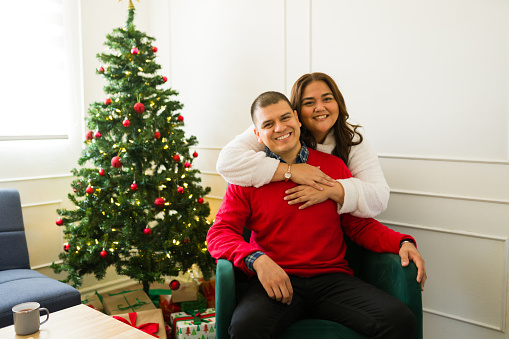 Mexican beautiful couple looking happy smiling and hugging while celebrating the christmas holidays together at home