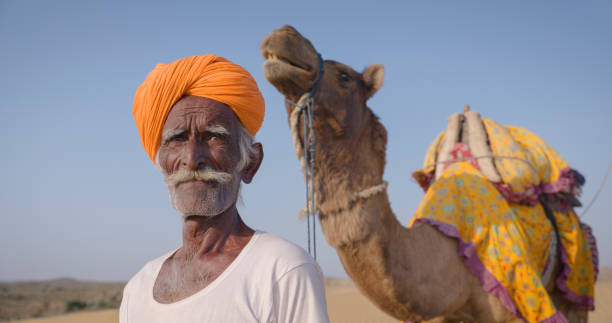 istock Indian man posing with camels on sand dunes, Rajasthan, India 1694385294