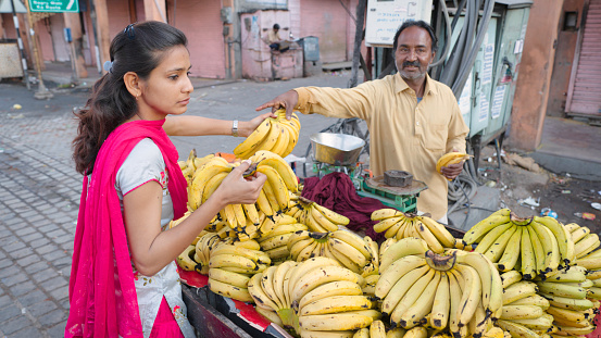 Young Indian woman buying bananas on the streets of The Pink City in Jaipur, Rajasthan, India. Jaipur is known as the Pink City, because of the color of the stone exclusively used for the construction of all the structures.