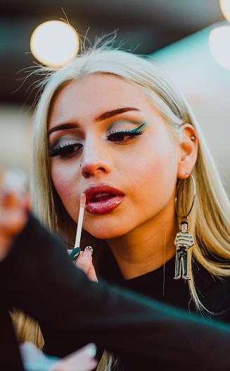 Close-up of stylish woman applying lip gloss while doing her makeup outdoors. Makeup and beauty concept.