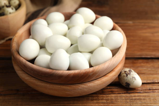 istock Many peeled boiled quail eggs and another one in shell on wooden table, closeup 1694455857