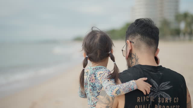 Rear view of Asian father and cute little daughter walking by the sea enjoying vacation together.