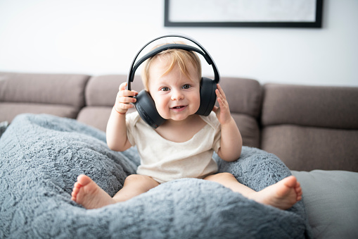 A portrait of a cute baby boy wearing big wireless headphones.