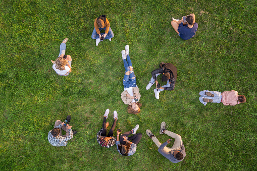 A large group of young teens sit in the grass during a break time, with their cell phones in hand, as they catch up on social media.  They are each dressed casually and focused on their individual screens.