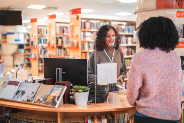 istock Hispanic Female Librarian In 50s Serving A Costumer 1694509388