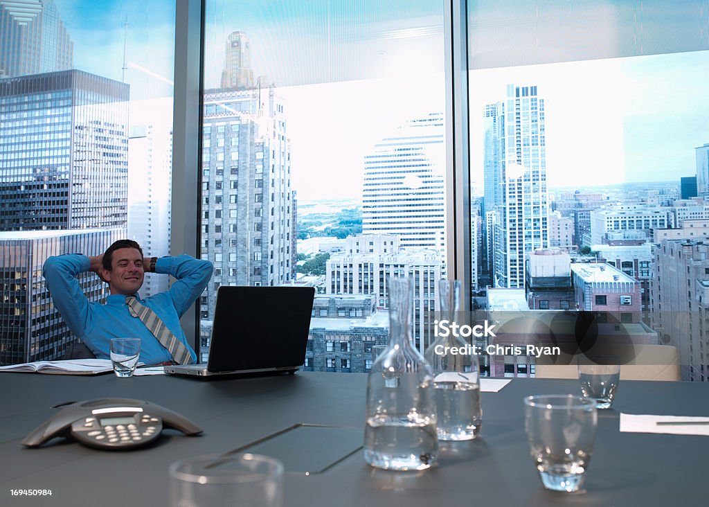 Sorridente empresário com as mãos atrás da cabeça na sala de conferências - Foto de stock de Felicidade royalty-free