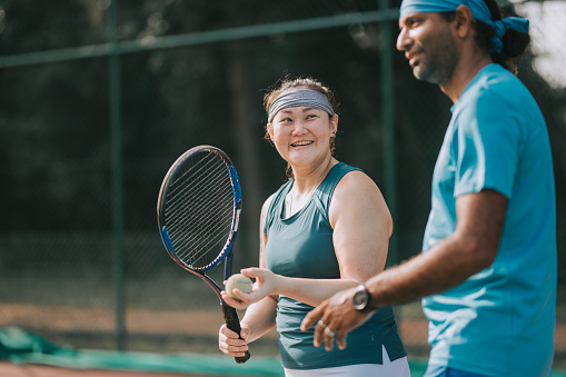 Asian Chinese mature adult woman learning tennis from her coach in tennis court during weekend morning