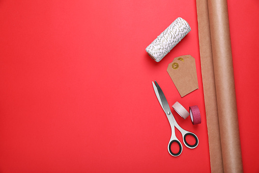 Roll of wrapping paper, scissors, tags and ribbons on red background, flat lay. Space for text