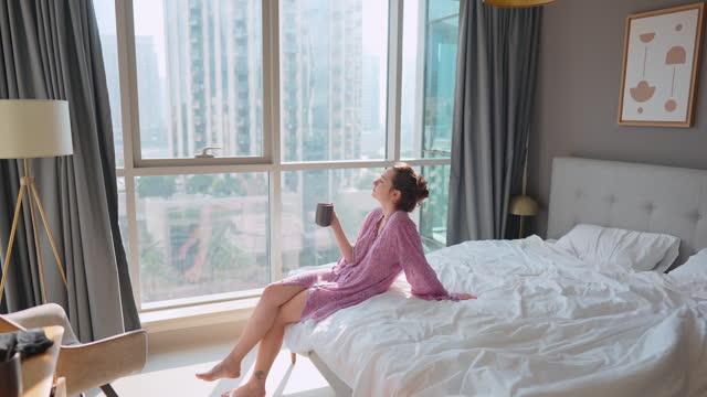 Woman sitting on bed and having a morning cup of coffee