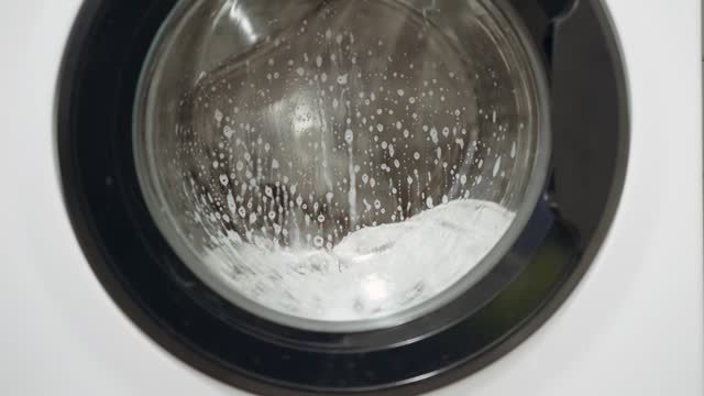 Water splashes in washing machine drum washing a dirty clothes, closeup, slow motion