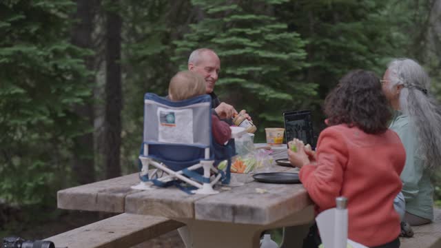 Multiracial multi-generation family eating lunch at campground picnic table