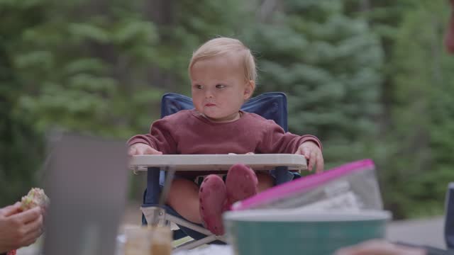 Baby bot eating in high chair while on family camping trip