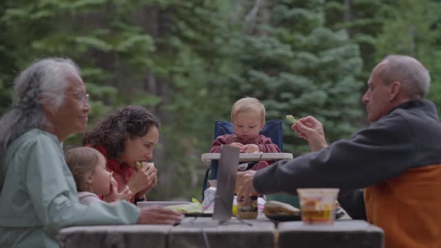 Multi-generation family eating meal together at campground picnic table