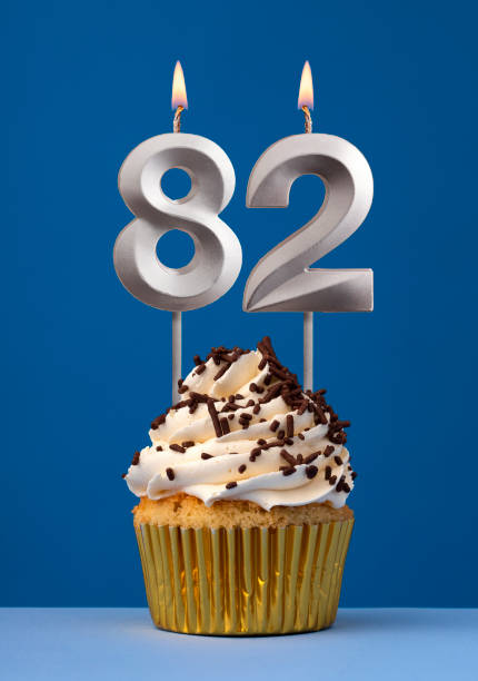 istock Burning candle number 82 - Birthday card with cake on blue Background 1694592600