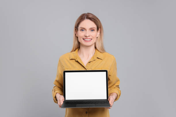 istock Happy woman showing laptop on light grey background 1694602750