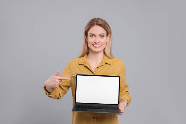 istock Happy woman showing laptop on light grey background 1694602818
