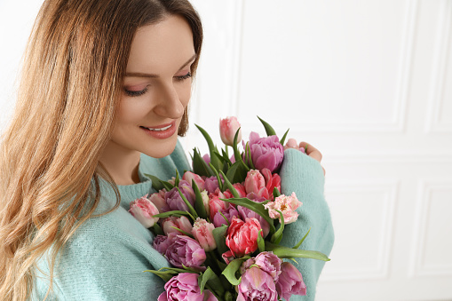 Young woman with bouquet of beautiful tulips indoors. Space for text