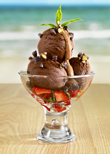 Cup of chocolate ice cream with fresh fruits on table at a tropical beach