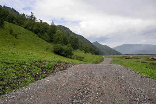 A country road between fields with hay bales in autumn in the mountains. Agricultural field with sky and clouds. The nature of agriculture. Straw in the meadow. Rural natural landscape.