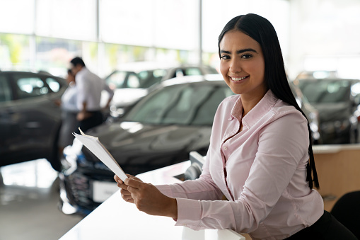 Portrait of a saleswoman working at a car dealership and looking at the camera smiling
