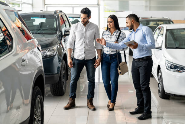 Salesman at the dealership showing a car to a couple Latin American salesman at the dealership showing a car to a couple interested in buying a vehicle - business concepts motor living stock pictures, royalty-free photos & images