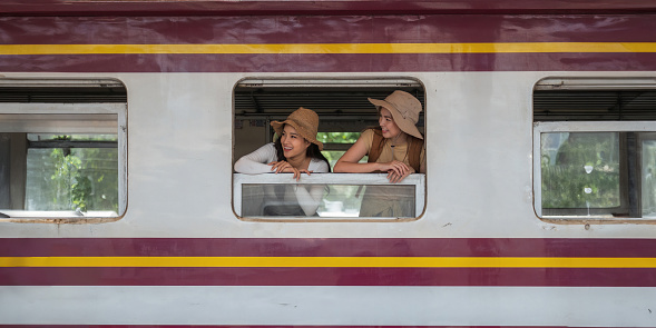 Happy smiling two woman looks out from window traveling by train on most picturesque train road concept