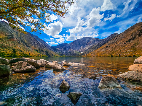 The iconic Convict Lake located high in the Eastern Sierra Mountains. Puffy white clouds dot a beautiful blue sky over the crystal clear water of the lake.The leaves on the waters edge are just starting to turn as fall approaches.