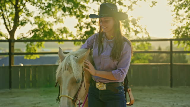 SLO MO Smiling Young Woman in Cowboy Hat Caressing Horse on Ranch Surrounded by Trees