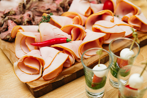 Slices of smoked ham on a wooden board. Thin slices of cold cuts and caprese canapes in shots. Close-up.
