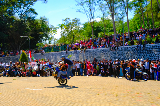 Bandung, West Java, Indonesia - 17 August, 2023 : The enthusiasm of residents watching motorbike stuntman attractions at Indonesia's 78th Independence Day Festival. A stuntman performing using a motorbike in the middle of the field.