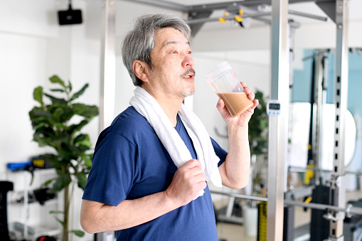 Asian gray-haired senior man drinking protein for training at the gym