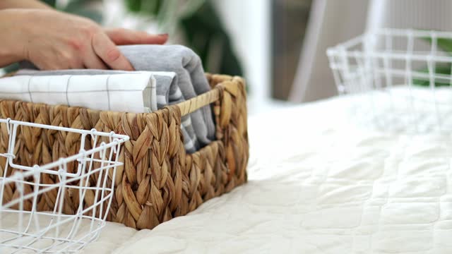The concept of storage and organization of space. Women's hands neatly fold T-shirts into a basket.