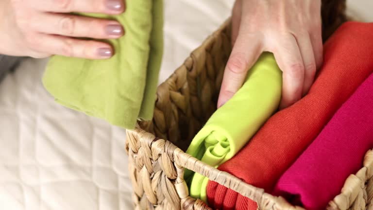 The concept of storage and organization of space. A woman vertically stacks T-shirts in a basket.