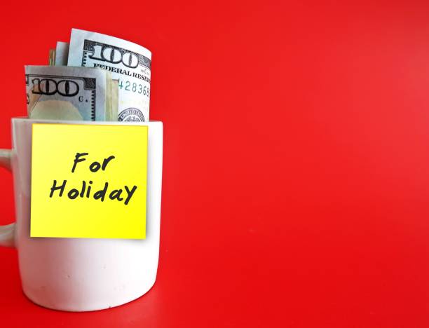 istock A white ceramic cup with cash dollars money inside and yellow sticky note with text written FOR HOLIDAY , on red background with copy space - concept of financial budget planning for coming holiday season 1694748410