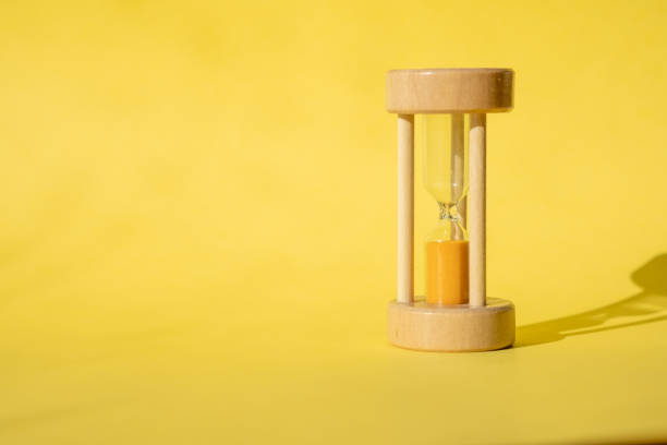 Hourglass, also known as sandglass, sand timer, sand clock. Time is running out concept. An hourglass with sand falling through, on a vibrant yellow background with copy space