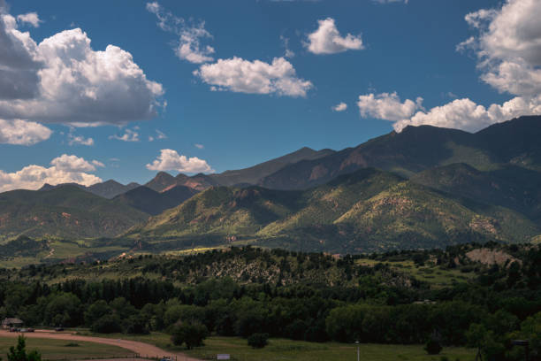 Sunlight washes over the lush foothills of America's Mountain, Pike's Peak in Colorado Springs, Colorado, while white puffy clouds drift overhead.