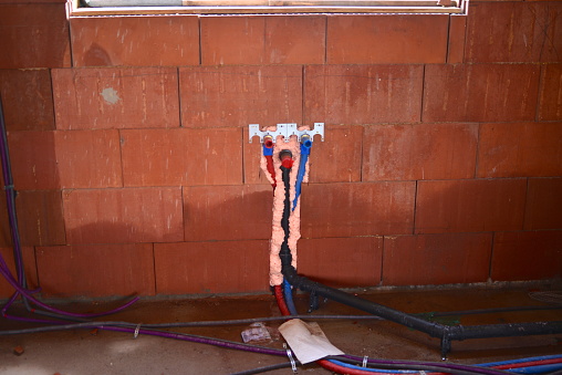 Installing all kinds of cabling and water pipes on the floor and walls, cables secured in the wall slot with expanding foam in new apartment under construction