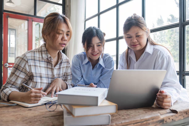istock Asian College groups of students using laptop, tablet, studying together with notebooks documents paper for report near windows in classroom. Happy young study for school assignment, Soft focus 1694872503