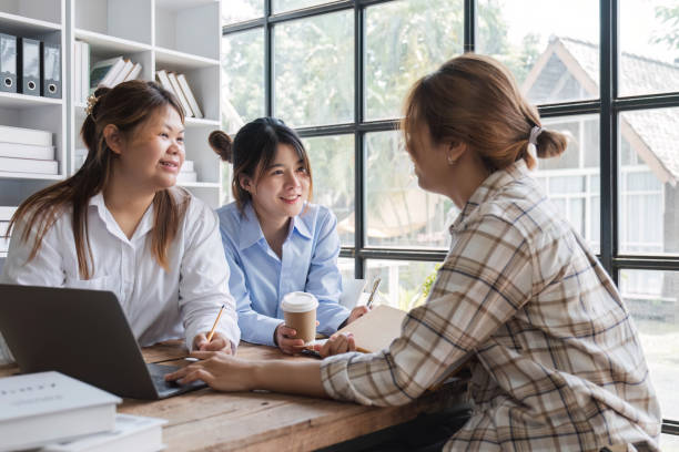 istock Asian College groups of students using laptop, tablet, studying together with notebooks documents paper for report near windows in classroom. Happy young study for school assignment, Soft focus 1694874108