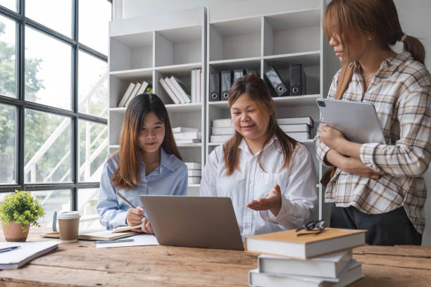 istock Asian College groups of students using laptop, tablet, studying together with notebooks documents paper for report near windows in classroom. Happy young study for school assignment, Soft focus 1694875724
